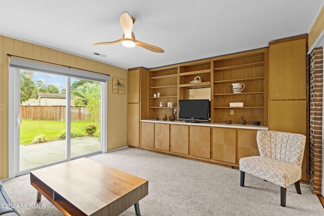 carpeted living room with wooden walls, a textured ceiling, and ceiling fan