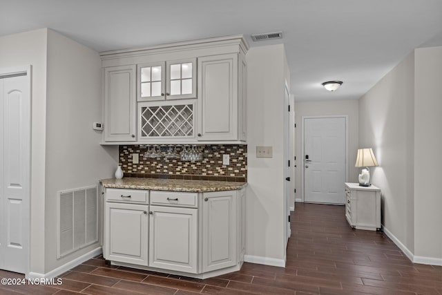 bar with dark wood-type flooring, light stone countertops, white cabinetry, and decorative backsplash