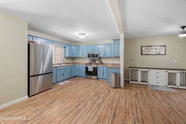 kitchen with stainless steel appliances, blue cabinetry, sink, and light wood-type flooring