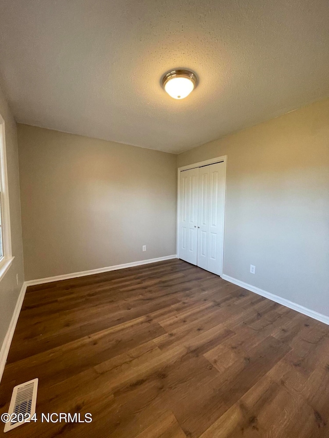 unfurnished bedroom with dark wood-type flooring, a closet, and a textured ceiling