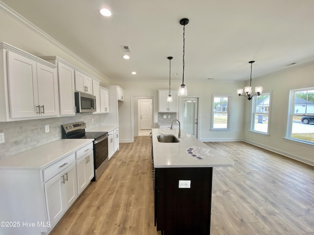 kitchen with decorative light fixtures, sink, white cabinets, stainless steel appliances, and a center island with sink