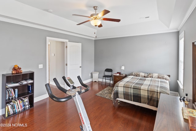 bedroom featuring ceiling fan, ornamental molding, a tray ceiling, and dark wood-type flooring