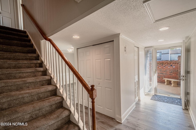 stairs featuring hardwood / wood-style flooring, crown molding, and a textured ceiling