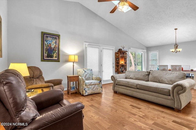 living room featuring a textured ceiling, high vaulted ceiling, ceiling fan with notable chandelier, and light wood-type flooring