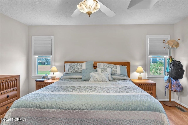 bedroom with a textured ceiling, wood-type flooring, and ceiling fan