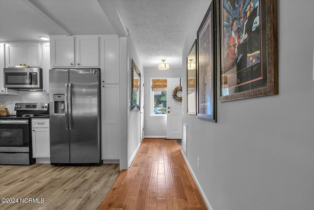 kitchen featuring appliances with stainless steel finishes, light hardwood / wood-style flooring, decorative backsplash, and white cabinets