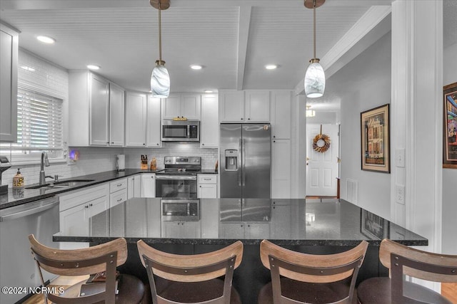 kitchen with appliances with stainless steel finishes, sink, dark stone counters, and pendant lighting