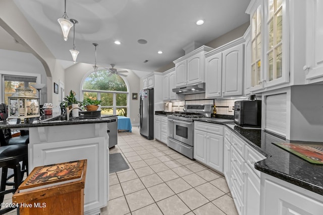 kitchen with appliances with stainless steel finishes, dark stone counters, ceiling fan, pendant lighting, and white cabinetry