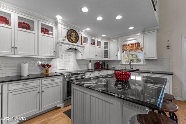 kitchen with a center island, light hardwood / wood-style floors, dark stone counters, a breakfast bar area, and electric range