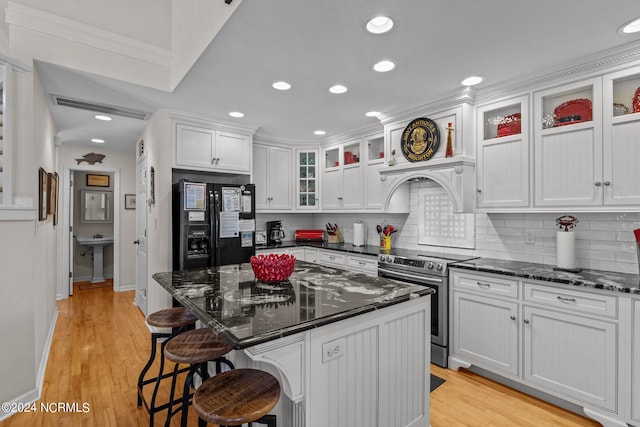 kitchen with dark stone counters, a kitchen island, light hardwood / wood-style flooring, a kitchen breakfast bar, and electric stove