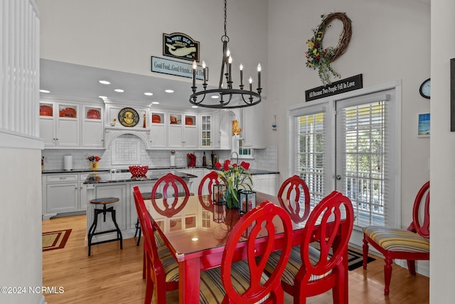 dining area with sink, a towering ceiling, an inviting chandelier, and light hardwood / wood-style flooring