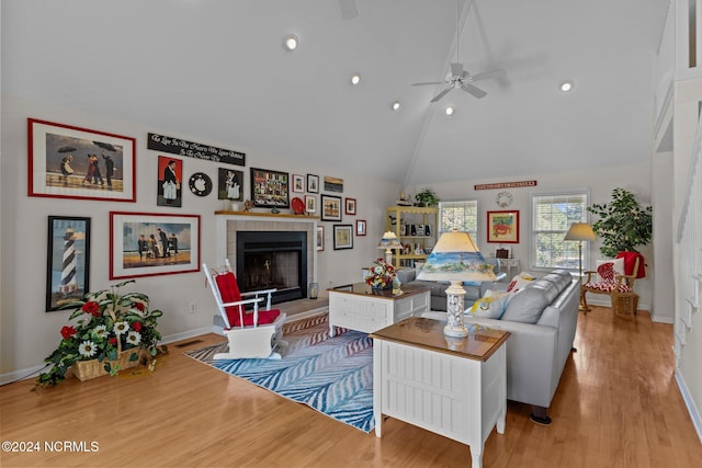 living room featuring ceiling fan, light hardwood / wood-style flooring, a tiled fireplace, and vaulted ceiling