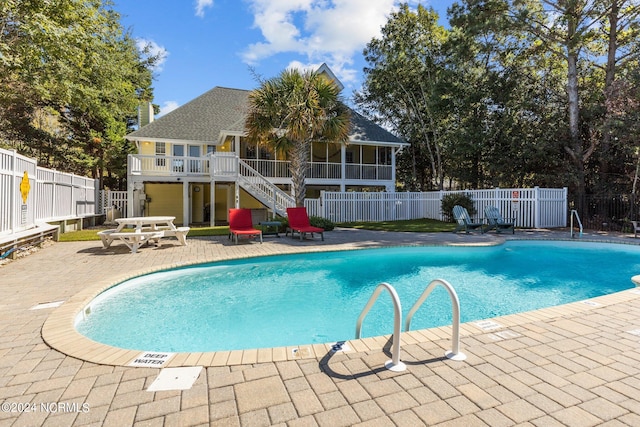 view of pool featuring a sunroom, a wooden deck, and a patio area