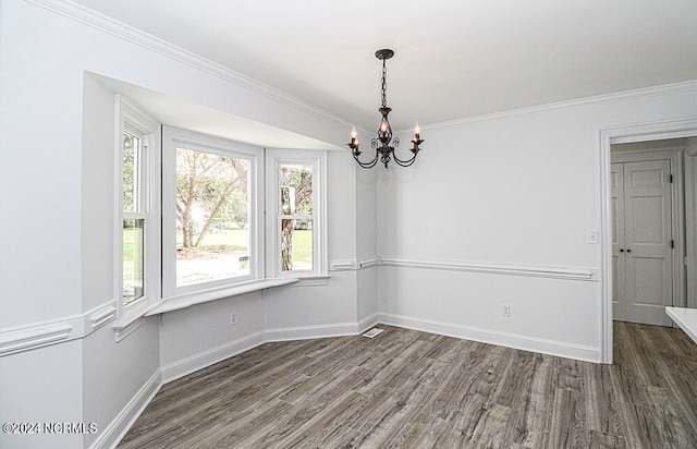 unfurnished dining area with dark wood-type flooring, ornamental molding, and an inviting chandelier