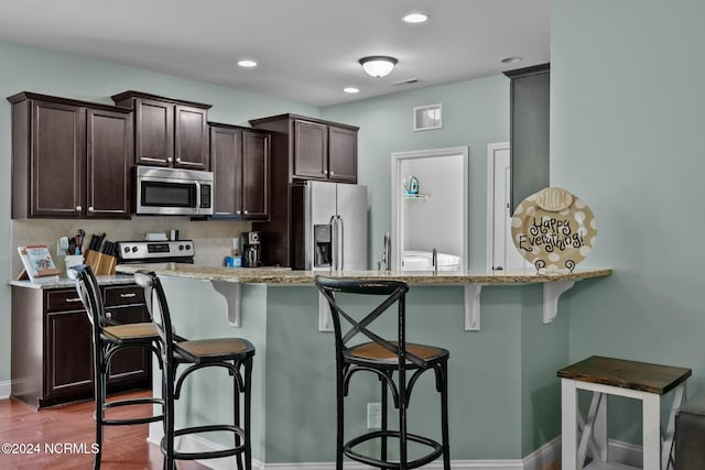 kitchen featuring appliances with stainless steel finishes, light stone countertops, hardwood / wood-style floors, and tasteful backsplash