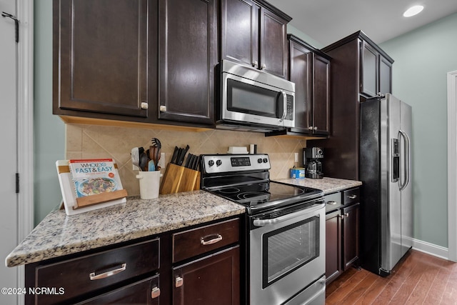 kitchen featuring light stone counters, dark brown cabinetry, decorative backsplash, dark wood-type flooring, and appliances with stainless steel finishes