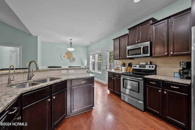 kitchen featuring light stone countertops, hardwood / wood-style floors, stainless steel appliances, sink, and decorative light fixtures