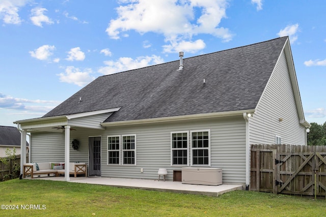 back of house with ceiling fan, a hot tub, a patio, outdoor lounge area, and a lawn