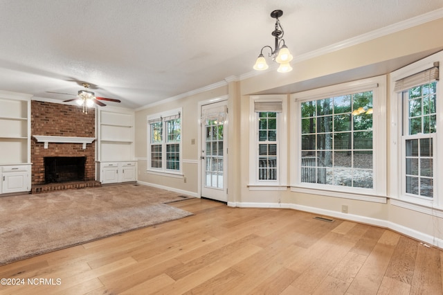 unfurnished living room featuring light wood-type flooring, ceiling fan with notable chandelier, a fireplace, a textured ceiling, and crown molding