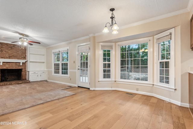 unfurnished living room with light hardwood / wood-style flooring, ornamental molding, a brick fireplace, a textured ceiling, and ceiling fan with notable chandelier