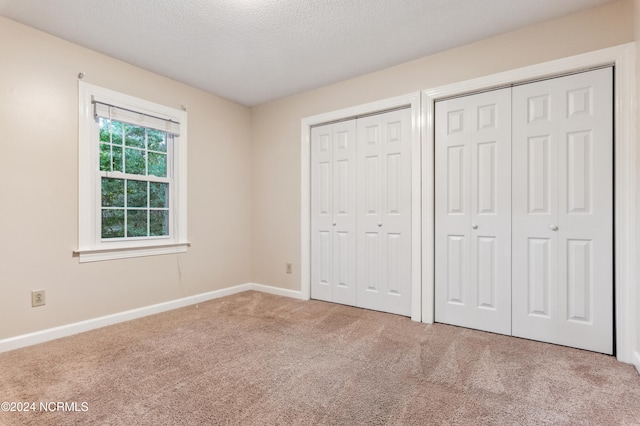 unfurnished bedroom with carpet floors, multiple closets, and a textured ceiling