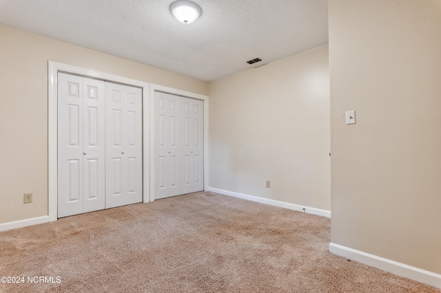 unfurnished bedroom featuring a textured ceiling, two closets, and carpet flooring