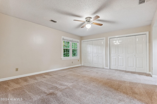 unfurnished bedroom featuring ceiling fan, multiple closets, a textured ceiling, and carpet floors