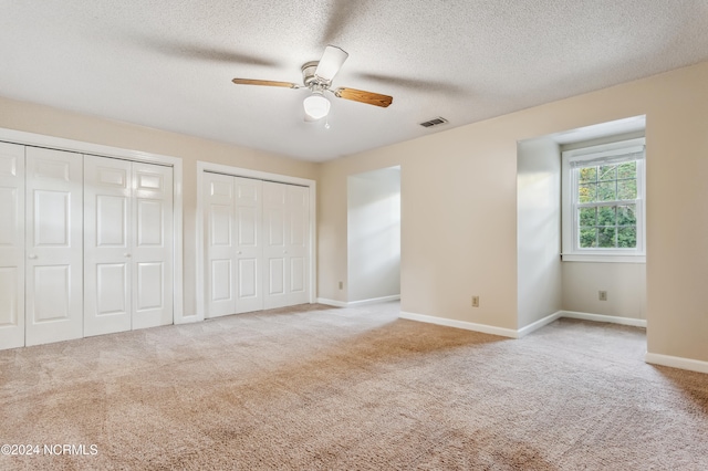 unfurnished bedroom featuring ceiling fan, light carpet, and multiple closets