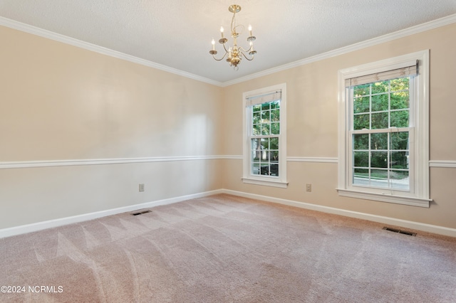 carpeted spare room with an inviting chandelier, ornamental molding, a textured ceiling, and a healthy amount of sunlight