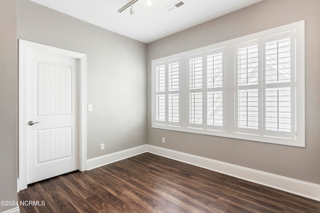 unfurnished room featuring track lighting, a healthy amount of sunlight, and dark wood-type flooring