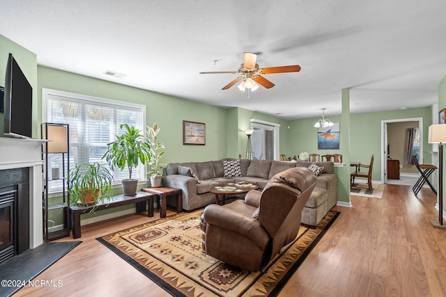 living room with ceiling fan with notable chandelier and light hardwood / wood-style flooring