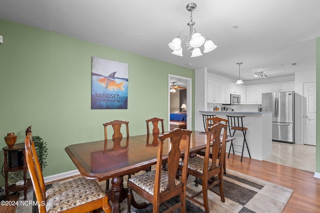 dining space with ceiling fan with notable chandelier and light hardwood / wood-style flooring