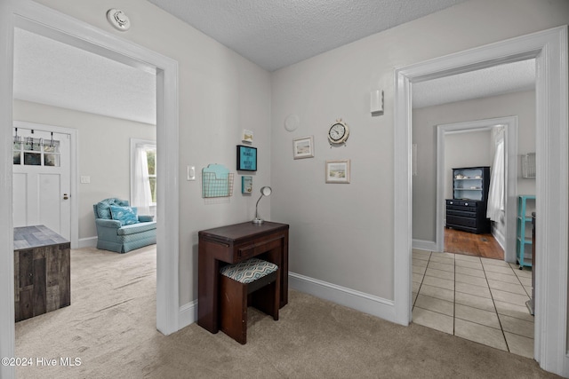 hall with a textured ceiling and light colored carpet