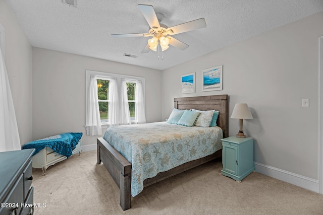 bedroom with a textured ceiling, light colored carpet, and ceiling fan