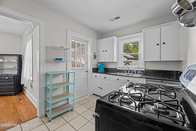 kitchen with white cabinets, sink, light wood-type flooring, and a textured ceiling