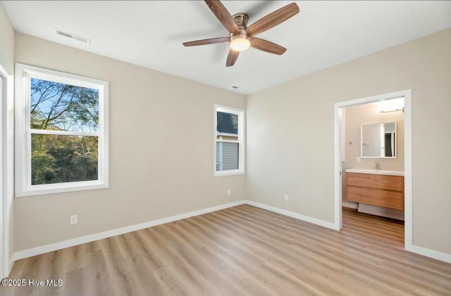 unfurnished bedroom featuring ceiling fan, light hardwood / wood-style floors, sink, and ensuite bath