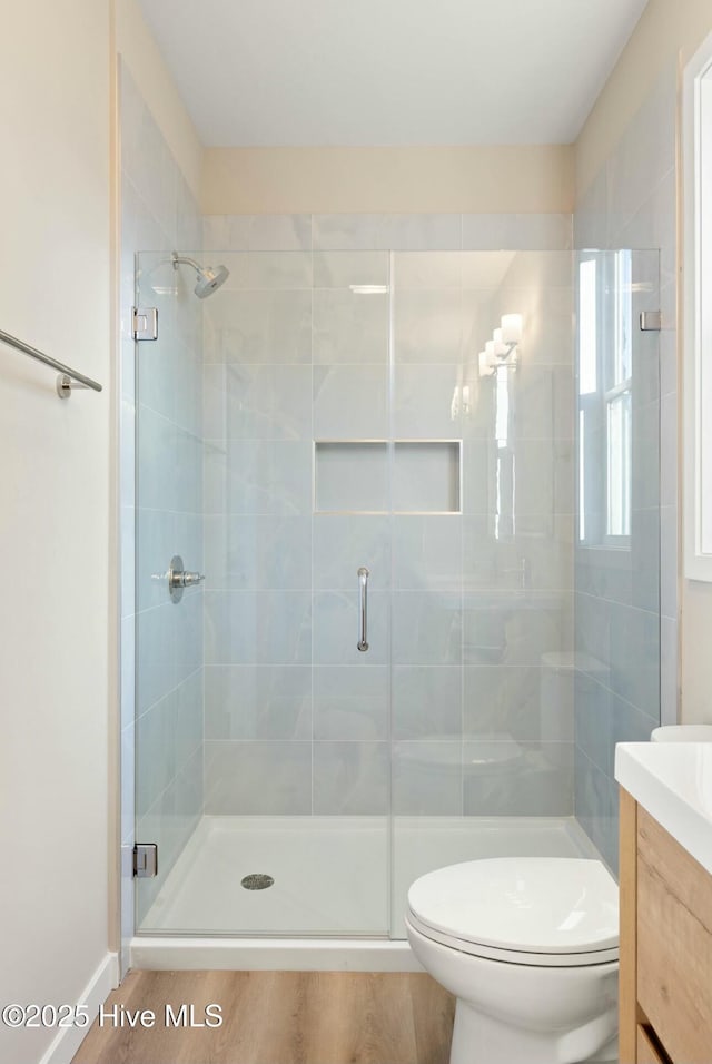 bathroom with hardwood / wood-style flooring, vanity, a shower with shower door, and toilet