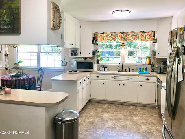 kitchen featuring white cabinets, appliances with stainless steel finishes, kitchen peninsula, and a wealth of natural light