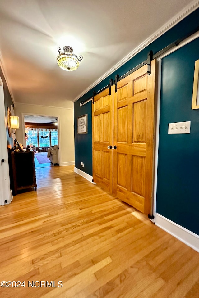 hall with a barn door, ornamental molding, and hardwood / wood-style floors