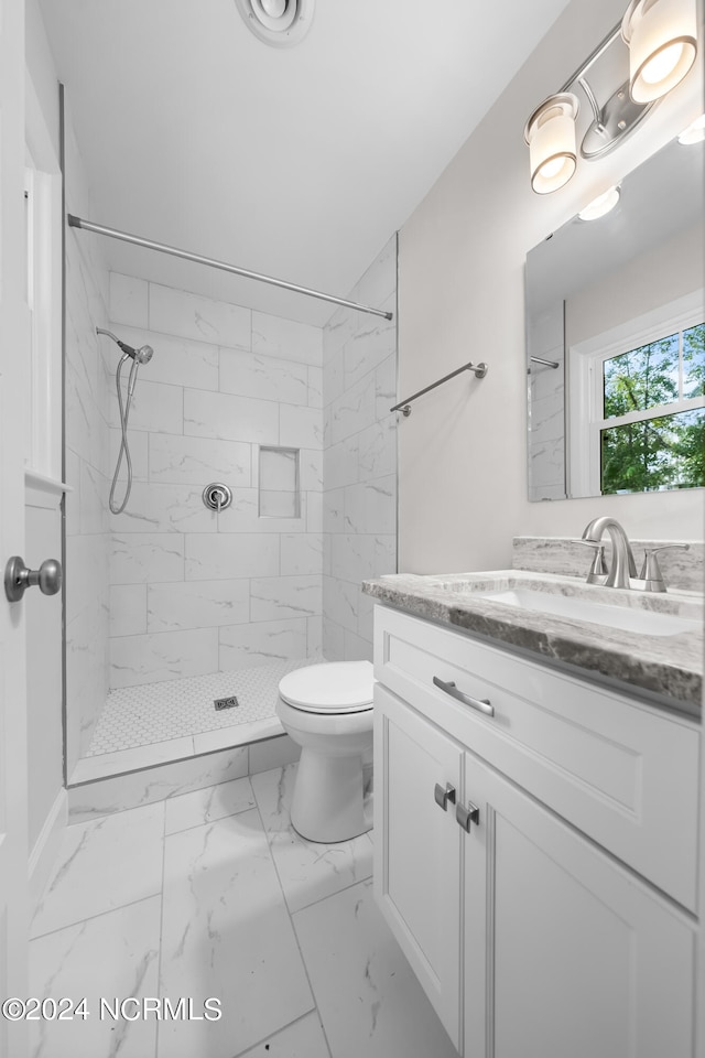 bathroom featuring a tile shower, vanity, and toilet