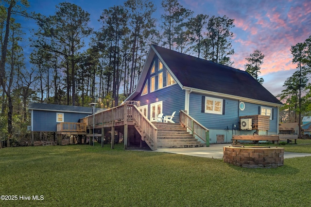 back of house at dusk with a deck, a lawn, and stairway