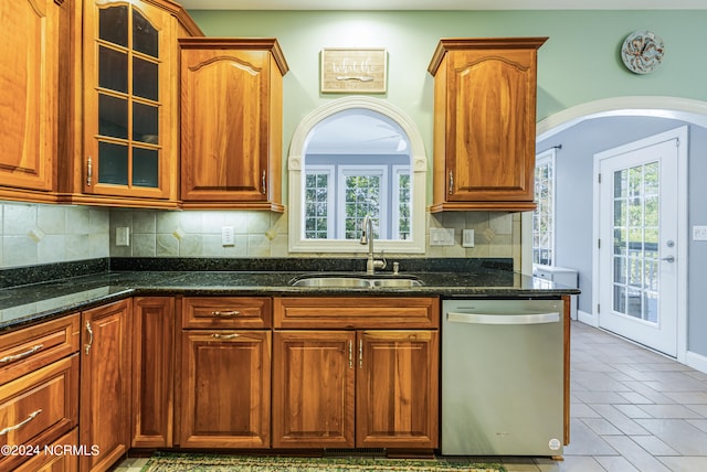 kitchen with dark stone counters, decorative backsplash, sink, and stainless steel dishwasher