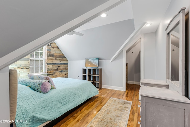 bedroom with lofted ceiling, wooden walls, and light wood-type flooring