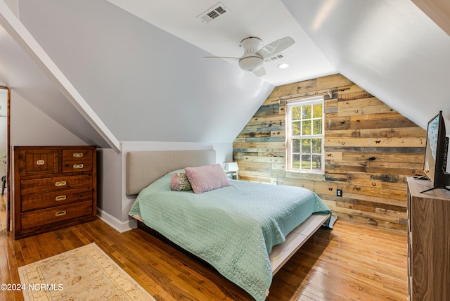 bedroom featuring lofted ceiling, wood walls, wood-type flooring, and ceiling fan