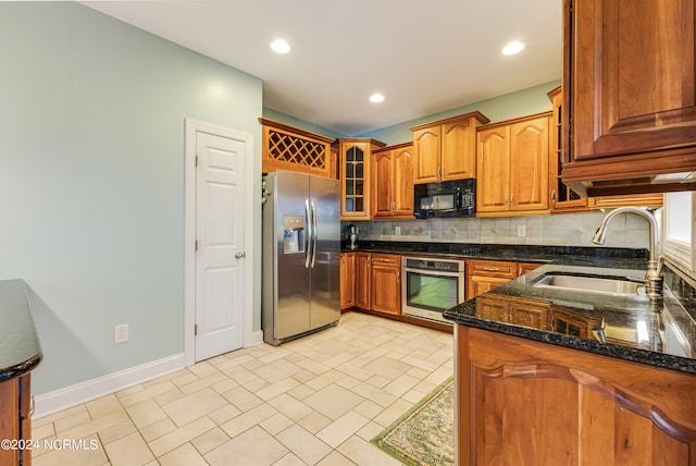 kitchen featuring kitchen peninsula, stainless steel appliances, backsplash, dark stone countertops, and sink