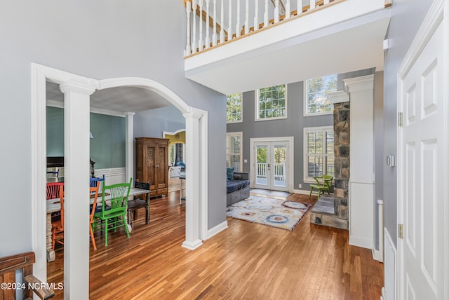 entryway with wood-type flooring, ornamental molding, ornate columns, a towering ceiling, and french doors