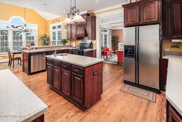 kitchen with appliances with stainless steel finishes, light hardwood / wood-style floors, decorative light fixtures, and an island with sink