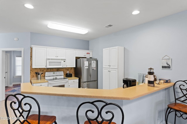 kitchen featuring white appliances, a breakfast bar area, and white cabinetry