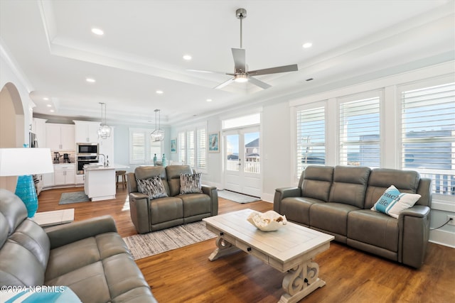 living room with a raised ceiling, recessed lighting, wood finished floors, and arched walkways