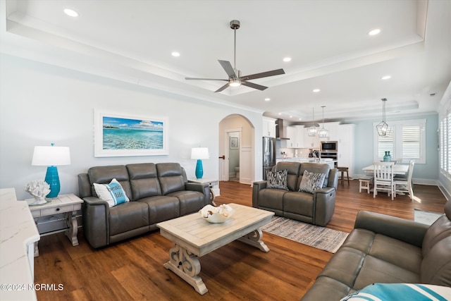 living room featuring arched walkways, dark wood-style floors, recessed lighting, and a raised ceiling